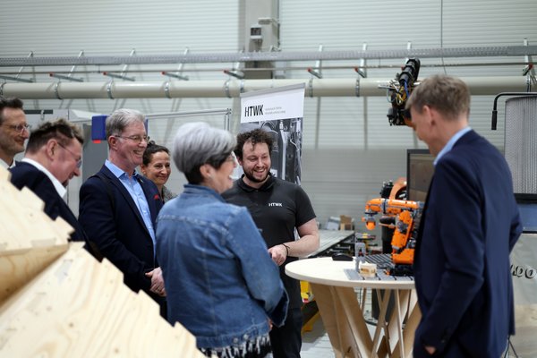 mehrere Personen schauen auf ein Robotermodell in einer Halle