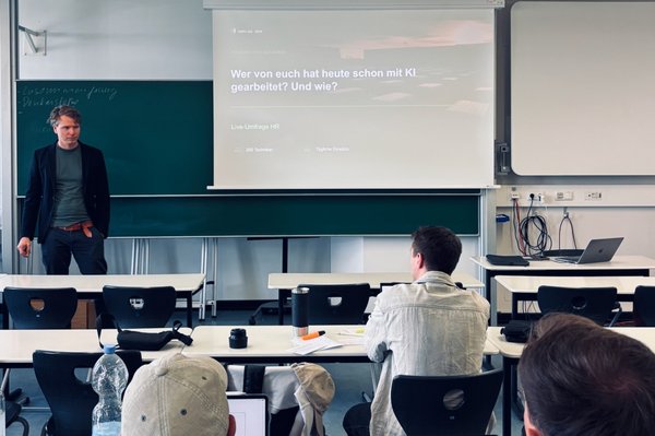 ozent steht in einem Seminarraum vor einer projizierten Präsentation auf einer Leinwand