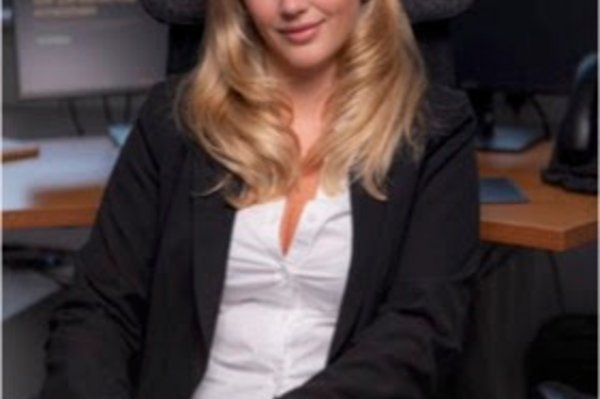 Interviewpartnerin Adelina Kuliqi sitzend in einem Büro, Blick zur Kamera